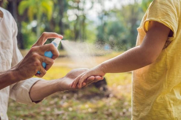 person spraying bug spray on kids arm