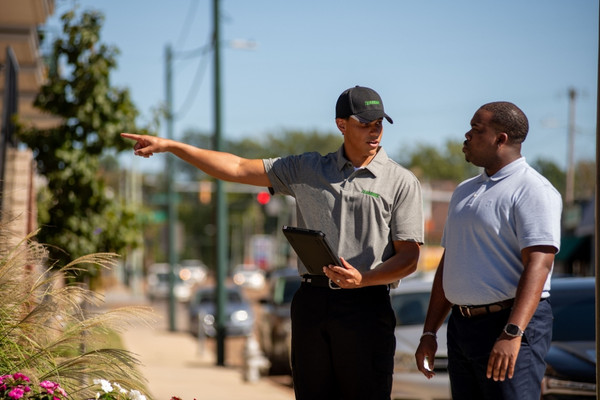 Pest control technician holding a tablet and pointing while talking with a customer outdoors