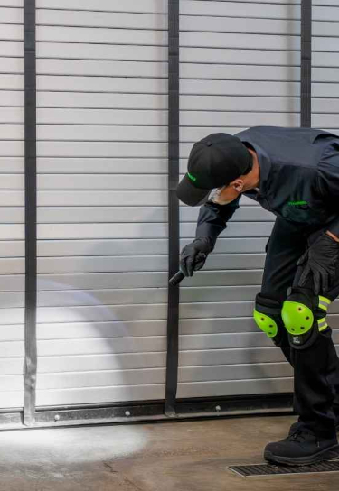 Pest control technician using a flashlight to inspect the bottom of a roll-up door