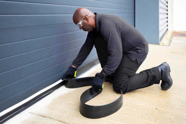 A Terminix technician installing Flexi Armour garage seal along a commercial garage door.