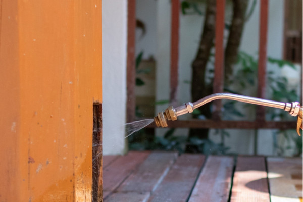 Close-up of a metal spray wand applying liquid repellent treatment to a wooden post.