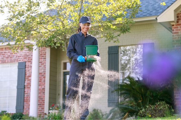 Pest control technician applying lawn granules outside a home