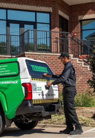 Terminix service technician opening the back of a service truck outside a brick building