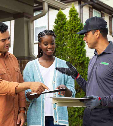 A technician, wearing protective gloves, speaks to a pair of customers