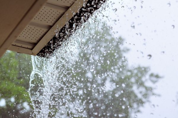 Heavy rain pouring over the edge of a roof gutter system lacking proper drainage